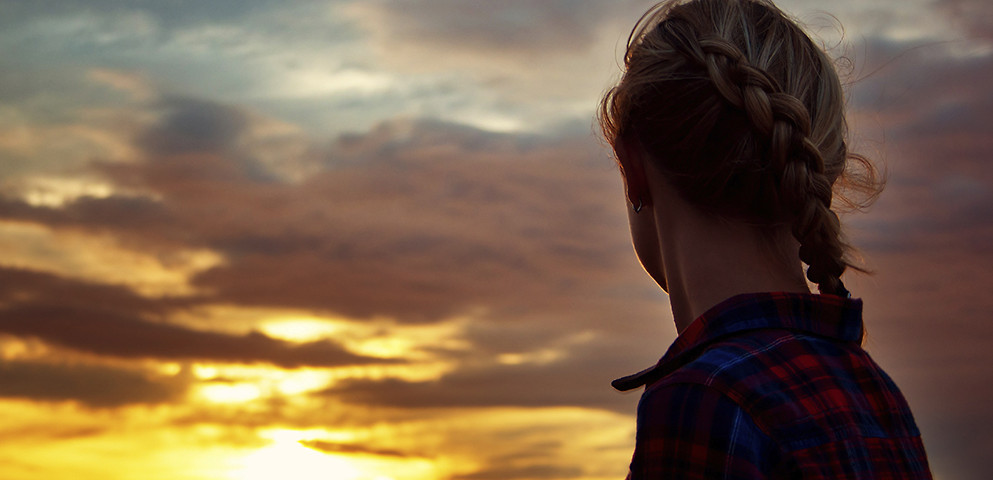 This is a decorative image. A woman turned away from the camera to look at a sunset.