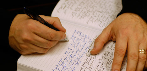 This image is decorative. A closeup of two hands, one writing in a journal.